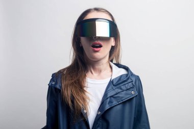 Sanal gerçeklik gözlüklü, açık arkaplanda mavi ceketli genç bir kadın..