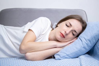 Sleeping young woman in white t-shirt lying on gray sofa.