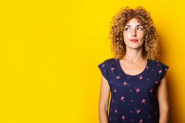 Kıvırcık genç bir kadın sarı arka planda dalgın dalgın bakıyor.