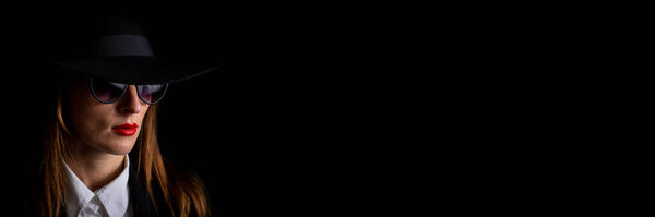 beautiful young business woman in a black hat and glasses on a black background. Banner.