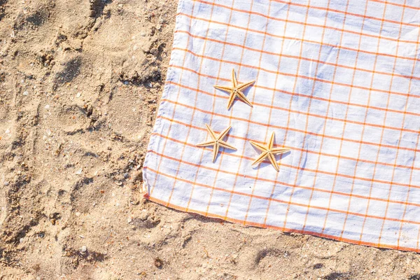 Kumlu bir sahilde, yatak örtüsünde altın denizyıldızı. Üst manzara, düz uzanma.