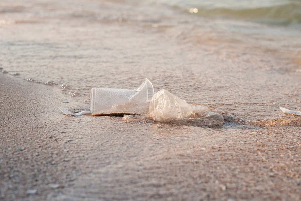 Plastic dishes and a plastic bag on the background of a sandy beach.