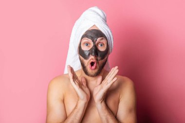 Pembe arka planda yüzünde kozmetik maske olan genç bir adam. Dikkat, temizlik..