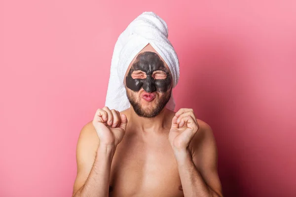 squint young man with a cosmetic mask on his face, with tightly closed eyes on a pink background. Skin care concept.