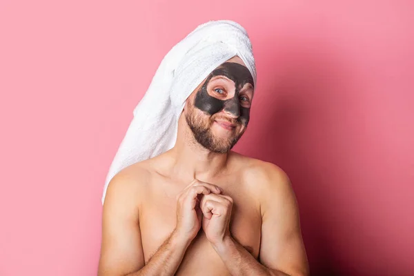 smiling young nude man with cosmetic mask on pink background. Skin care concept.