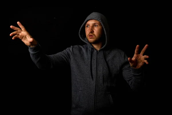 Man in a hood is touching something on a dark background.