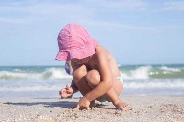 Child blond girl is played with sand on the beach