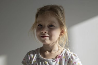 Gülümseyen güzel bir kız çocuğu dağınık saçlı beyaz bir duvarın arkasında