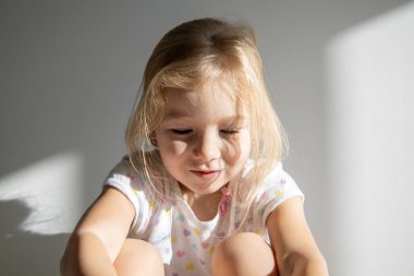 Beyaz bir duvarın arkasında dağınık saçlı üzgün bir kız çocuğu.