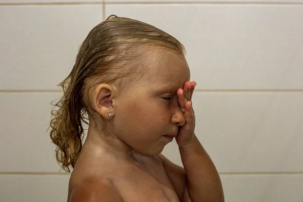 Child girl with closed eyes with wet hair takes a shower