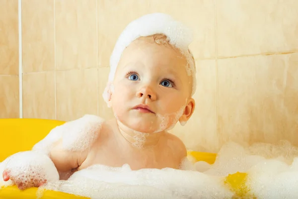 小さな赤ちゃんは泡と泡で黄色のバスルームでお風呂に入ります 幸せな子供の概念 入浴への愛 — ストック写真