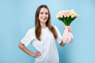 Elinde mavi arka planda laleleri olan gülümseyen genç bir kadın..