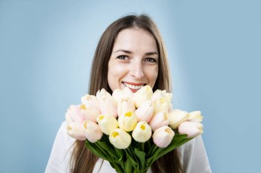 Gülümseyen genç kadın mavi arka planda bir buket lale tutuyor..