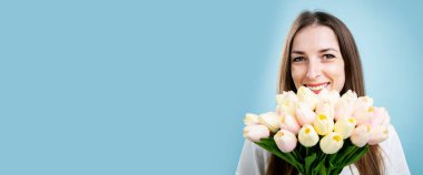 Mavi arka planda elinde bir buket lale tutan gülümseyen genç kadın. Pankart.