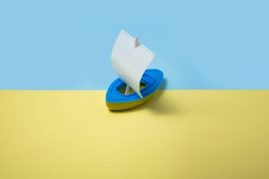 Sarı-mavi arka planda plastik oyuncak gemi. Üst görünüm, düz uzanma.