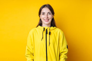 Sarı arka planda, sarı ceketli, gülümseyen genç kadın..