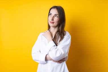 Sarı arka planda beyaz gömlekli dalgın, güzel bir kadın..