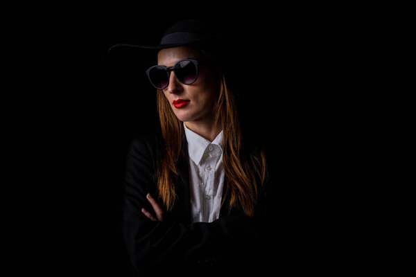 beautiful business elegant woman in a black hat, glasses on a black background.