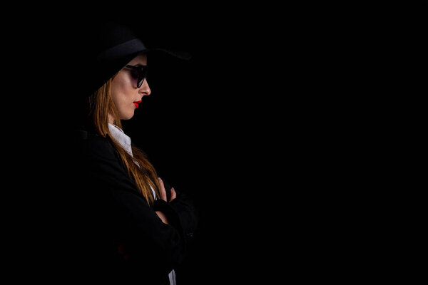 beautiful business elegant woman in profile, in a black hat, in glasses on a black background.
