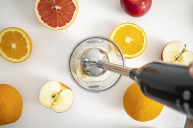 Siyah el blenderi mutfaktaki bir kasede taze meyve karıştırır. Üst manzara, düz uzanma.