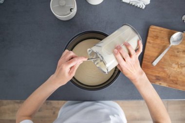 Kadın kaseden yemek kabına hamur döküyor. Üst manzara, düz uzanma.