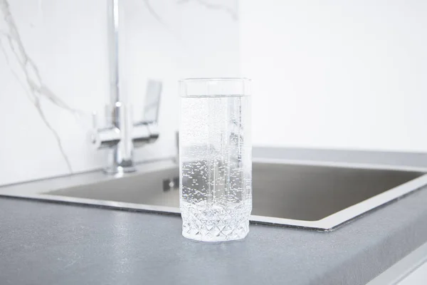 Glass of water stands on the countertop near the sink in the kitchen.