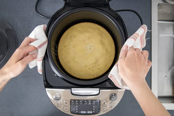 Women\'s hands reach out to get a baked pie from a multicooker. Top view, flat lay.