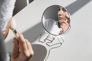 Young woman without makeup doing face massage with roller massager.