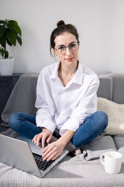 Dizüstü bilgisayarlı, kanepede kahve içen genç bir kadın.