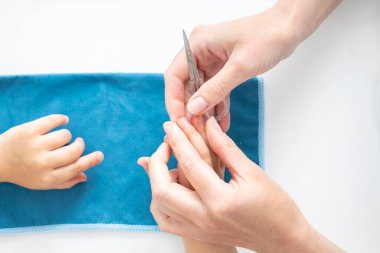 Children's manicure. Female hands cut nails on children's hands with manicure scissors. Top view, flat lay.