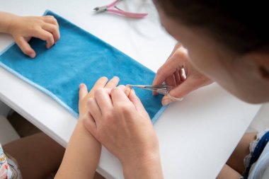 Mom does a manicure to her daughter cuts nails with nail scissors at home