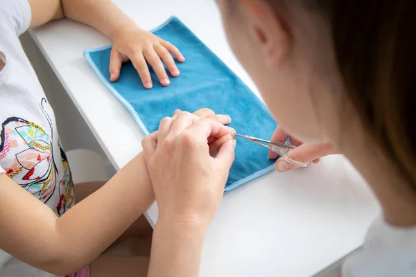 Children\'s manicure. Mom cuts off her daughter\'s nails with nail scissors at home.