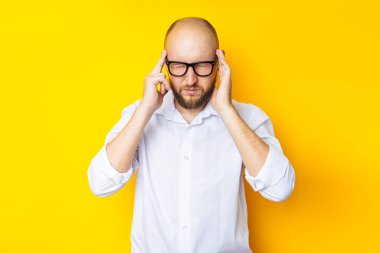 Young man squinting holding on to the weights on his head on a yellow background.