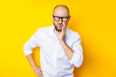 Young man squinting holding his cheek on a yellow background.