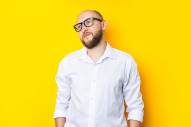 Pensive bearded young man in glasses in a shirt on a yellow background
