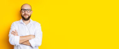 Man bald with a beard in glasses in a white shirt on a yellow background. Banner.
