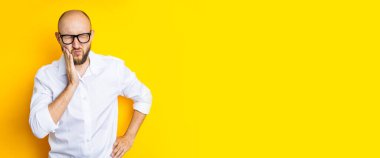 Young man squinting holding his cheek on a yellow background. Banner.