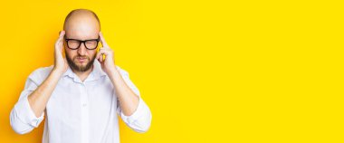Young man squinting holding on to the weights on his head on a yellow background. Banner.