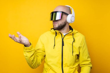 Young man in cyberpunk glasses with headphones holding an invisible object on a yellow background.