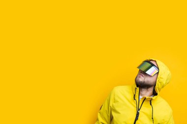 Young man in virtual reality glasses looking up on yellow background.