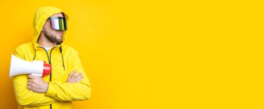 Young man in cyberpunk glasses holding a megaphone on a yellow background. Banner.