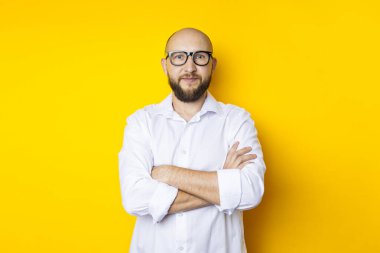 Man bald with a beard in glasses in a white shirt on a yellow background.