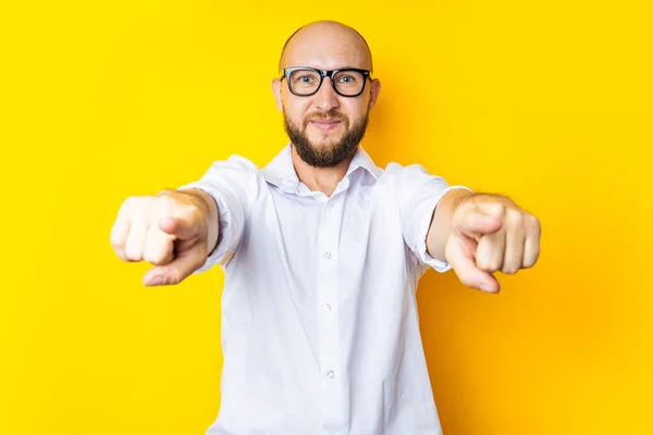 Smiling young man pointing fingers at viewer on yellow background.