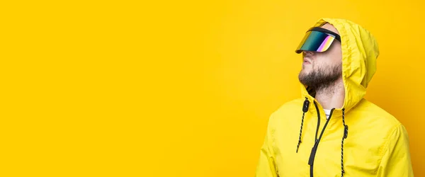Young man in cyberpunk glasses in a yellow jacket looks up on a yellow background. Banner.