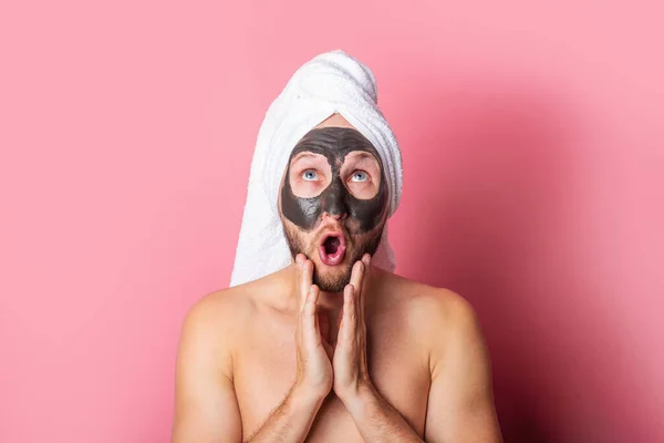 surprised young man with cosmetic mask on his face on pink background. Care, cleaning.