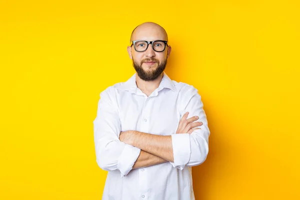Man bald with a beard in glasses in a white shirt on a yellow background.