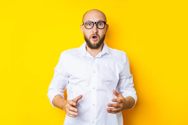 Frightened young man with a beard in glasses on a yellow background.