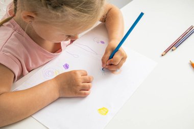 A child blonde girl draws with colored pencils sitting at the table. Top view, flat lay.