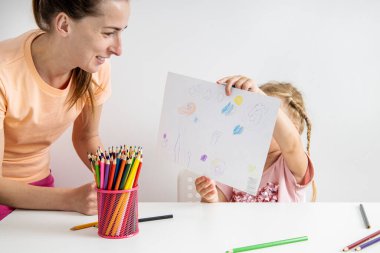 Child girl shows a drawn drawing with colored pencils on paper.