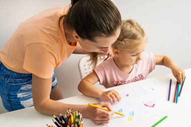 Drawing teacher helps child girl to draw with colored pencils on paper.